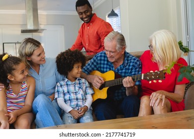 Happy multiracial multigeneration family looking at senior man playing guitar while sitting on sofa. Unaltered, family, togetherness, childhood, retirement, music, hobbies, lifestyle and home. - Powered by Shutterstock