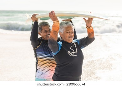 Happy multiracial senior couple carrying surfboard on heads against sea at beach during sunny day. water sport and active lifestyle. - Powered by Shutterstock