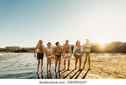 Happy multiracial senior friends having fun walking on the beach at sunset during summer holidays - Diverse elderly people enjoying vacations - Powered by Shutterstock