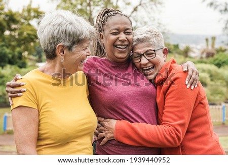Happy multiracial senior women having fun together outdoor - Elderly generation people hugging each other at park