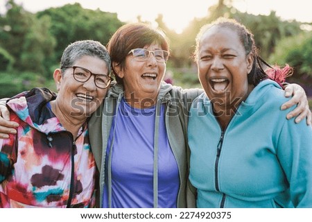 Happy multiracial senior women having fun together outdoor - Elderly generation people hugging each other at city park with sunrise in the background