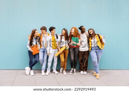 Happy multiracial students standing over isolated blue background. Diverse teenage friends having fun talking leaning on campus building college wall