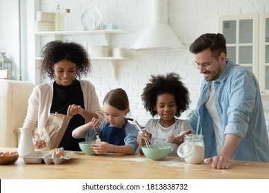 Happy multiracial young couple involved in cooking pastry with adorable mixed race daughters in modern kitchen. Smiling diverse family preparing homemade sweets or pancakes for breakfast at weekend. - Powered by Shutterstock