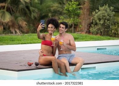 Happy multiracial young couple taking selfie in swimming pool at resort. Healthy and technology lifestyle with young people drinking fruit juice and eating some fruits.  - Powered by Shutterstock