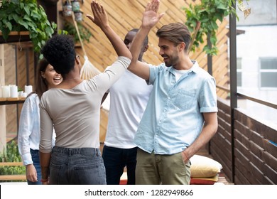 Happy multiracial young people wearing casual clothes standing in summer cafe cozy terrace greeting each other with hand gesture giving high five, showing unity togetherness, celebrating graduation - Shutterstock ID 1282949866