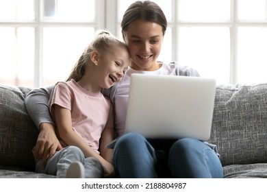 Happy Mum And Cute Gen Z Kid Watching Funny Movie On Laptop At Home. Smiling Mother And Daughter Girl Using Pc Device, Talking To Family Via Video Call, Shopping Online, Playing Games On Internet