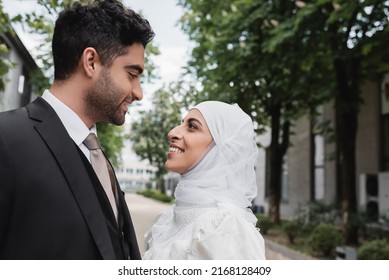 happy muslim bride in white hijab and groom in suit looking at each other