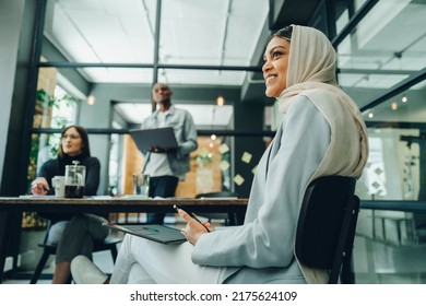 Happy Muslim Businesswoman Holding Wireless Technology While Sitting In An Office Meeting. Cheerful Young Businesswoman Wearing A Hijab In An Inclusive Workplace.