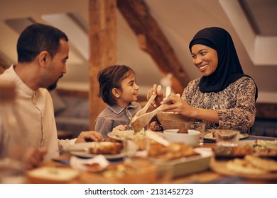 Happy Muslim family enjoying in conversation while having dinner together at dining table on Ramadan. Focus is on mother and daughter.