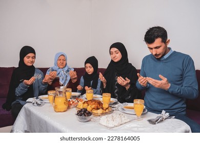 Happy Muslim family making iftar dua to break fasting during Ramadan parents having dinner with their children and grandmother at dining table at home gathering and feasting. - Powered by Shutterstock