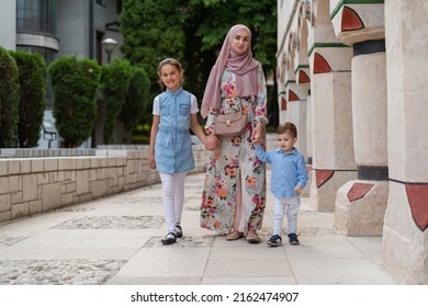 Happy Muslim Family Mom In Hijab Walking And Holding Hands With Two Children Outdoor.	