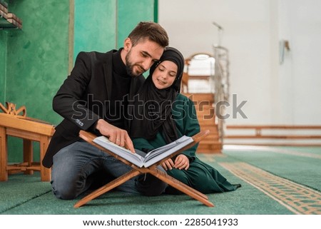 A happy Muslim family young father with child daughter reading a Quran inside the Mosque.