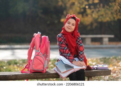 A Happy Muslim Girl Student Learning For School In The Autumn Park.