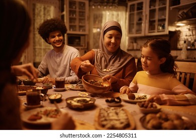 Happy Muslim grandmother serving food to her granddaughter during family dinner at dining table. - Powered by Shutterstock