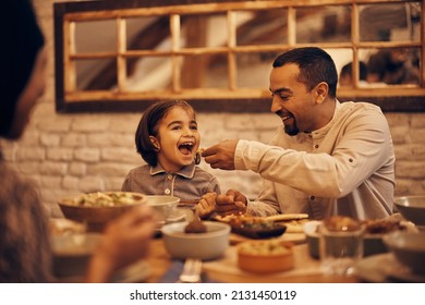 Happy Muslim little girl having fun while father is feeding her while having dinner at home on Ramadan. 
