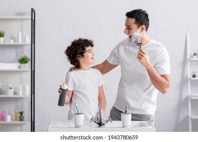 Happy muslim man shaving beard and hugging son with foam in bathroom - Powered by Shutterstock