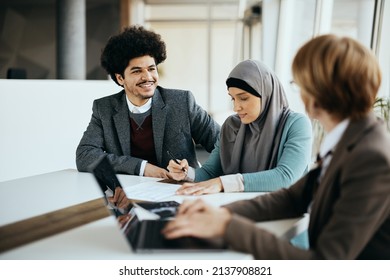 Happy Muslim Man Talking To Financial Advisor While His Wife Is Signing Paperwork During The Meeting In The Office. 