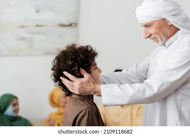 happy muslim man in turban hugging head of arabian grandson near blurred multiethnic family