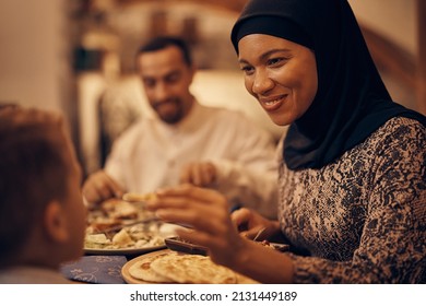 Happy Muslim mother feeding her son while having family dinner in dining room.