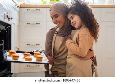 Happy muslim mother and her little daughter baking together in kitchen, taking tray with fresh muffins out of oven. Islamic mom and child enjoying smell of homemade pastry, closeup shot - Powered by Shutterstock