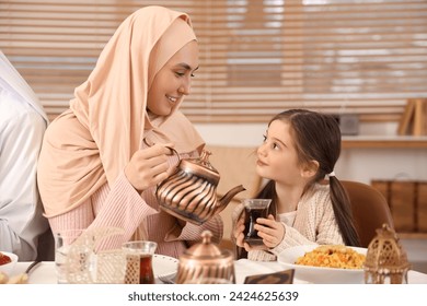 Happy Muslim mother pouring tea for her little daughter at family dinner. Ramadan celebration - Powered by Shutterstock