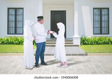 Happy Muslim Parents Giving Money Envelope To Her Daughter During Eid Mubarak While Standing In Front Of House