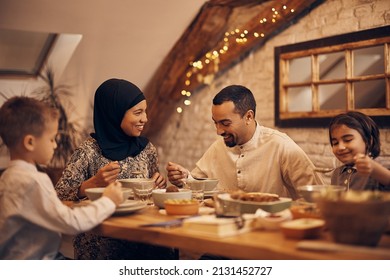 Happy Muslim parents having evening meal with their kids at dining table at home. 