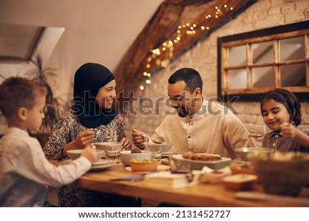 Happy Muslim parents having evening meal with their kids at dining table at home. 