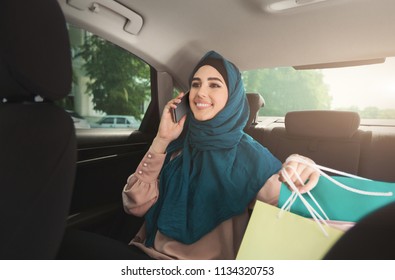 Happy Muslim Woman Talking On Smartphone With Shopping Bags In Car