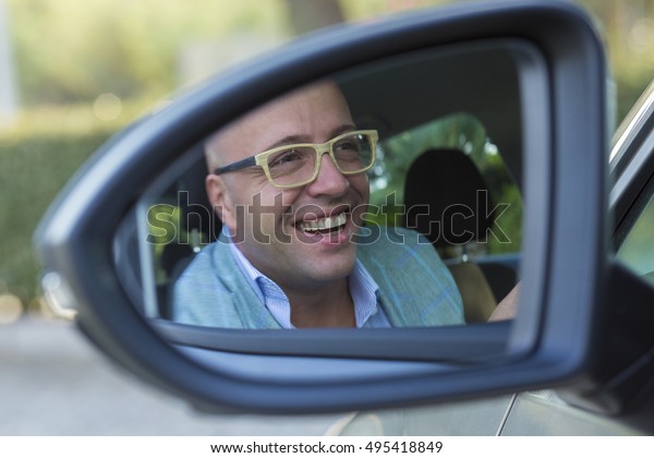 Happy with my car choice. Portrait young man\
driver reflection in car side view mirror. Guy driving his new car.\
Positive human face expression emotions. Safe trip journey driving\
concept