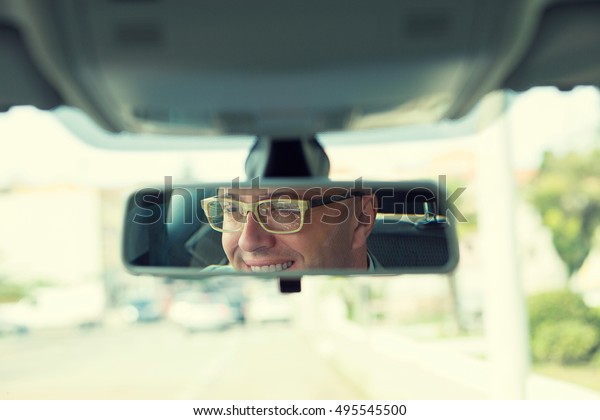 Happy with my car choice. Portrait young man\
driver reflection in car rear view mirror. Guy driving his new car.\
Positive human face expression emotions. Safe trip journey driving\
concept