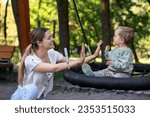 Happy nanny and cute little boy on swing outdoors