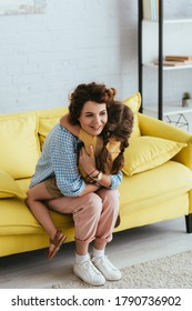 Happy Nanny Hugging Child While Sitting On Yellow Sofa