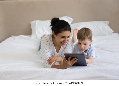 Happy nanny and kid watching movie, media content on tablet together, lying, resting in bed, looking at digital gadget screen, laughing. Mom teaching kid to read, using online learning app - Powered by Shutterstock