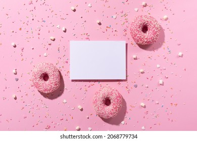 Happy National donut or doughnut day concept. Donuts with pink icing, sugar sprinkle and emtpy white paper sheet  on pink background. Top view, copy space.