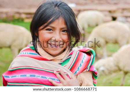 Happy native american girl wearing ethnic aymara cloth. Sheep on the background.