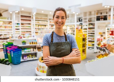 Fröhliche junge Verkaufsfrau im modernen Supermarkt. Waffen überqueren. Blickkamera
