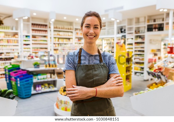 Happy natural young saleswoman in modern\
supermarket. Cross arms. Looking\
camera