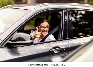 A Happy Nerdy Girl Is Driving A Car And Showing Thumbs Up To Other Drivers. It Is Not Hard To Be Polite In Traffic. A Girl Driving A Car