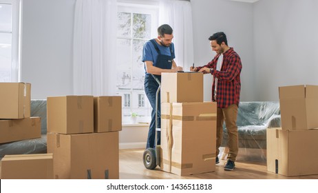 Happy New Homeowner Welcomes Professional Mover with Hand Truck full of Cardboard Boxes, Receives His Goods and Signs on Clipboard.