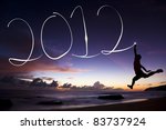 happy new year 2012. young man jumping and drawing 2012 by flashlight in the air on the beach before sunrise