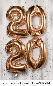 Happy New year 2020 celebration. Bright gold balloons figures, New Year Balloons with glitter stars on wood white background. Christmas and new year celebration. Gold foil balloons 2020
