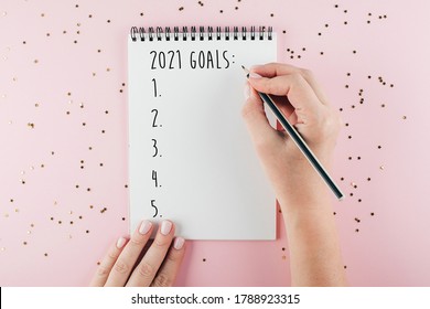 Happy New Year 2021. Woman's hand writing 2020 Goals in notebook decorated with Christmas decorations on the tricolor background. Top view, flat lay - Powered by Shutterstock