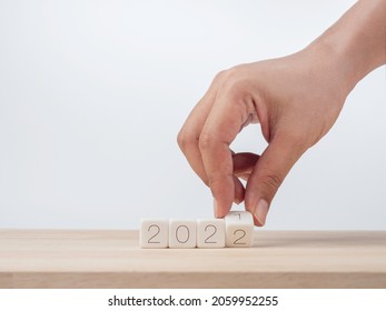 Happy New Year, 2022 Background Concept. Close-up Hand Flipping Wooden Cube Blocks For Change Number From 2021 To The New Year 2022 On The Desk On White Background, Clean, Modern, And Minimal Style.