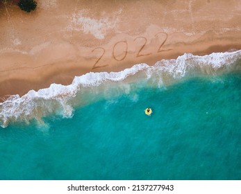 Happy New Year 2022, lettering on the beach with wave and blue sea. Numbers 2022 year on the sea shore, New Years concept.
