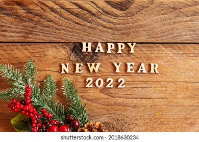 Happy New Year 2022. Quote made from wooden letters and numbers 2022 on wooden background dcorated fir tree branch with berries and cones. Creative concept for new year greeting card