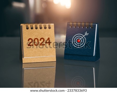 Happy new year 2024 banner background. 2024 number year with target icon on brown and blue small desk calendar cover standing on glass table with new day sunlight. Business goals and success concepts.