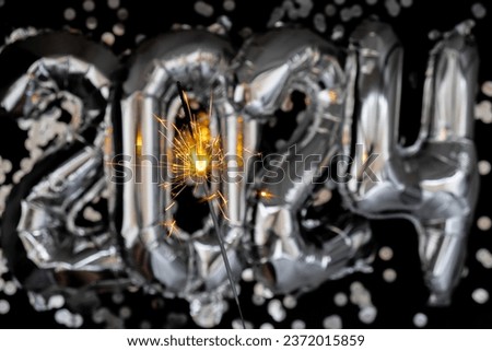 Happy new year 2024 metallic balloons with confetti and sparkler firework Bengal lights on dark black background. Greeting card silver foil balloons numbers Christmas holiday concept. Celebration