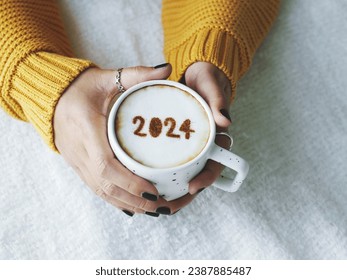 Happy New Year 2024 theme number 2024 over frothy surface of cappuccino served in white coffee mug holding by female hands on bed with white blanket background. Holidays food art, new year new you. - Powered by Shutterstock