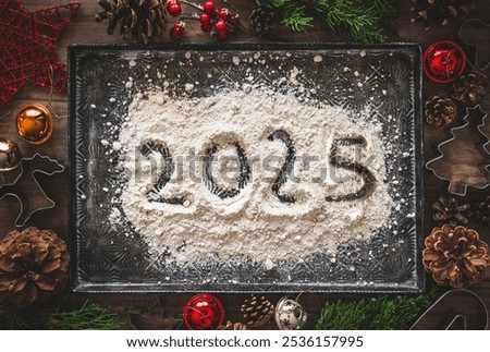 Happy new year 2025 concept. A baking tray with a pile of flour with the number 2025 written on it, surrounded by Christmas decorations and cookie cutters. 